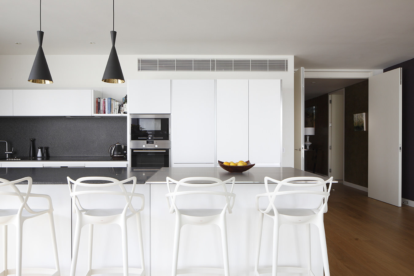 Contemporary kitchen with handleless white units, granite splashback and black pendants